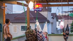A room with a view of houses through a window, a hammock, and a person standing. - Karma Home Hostel (Phitsanulok)