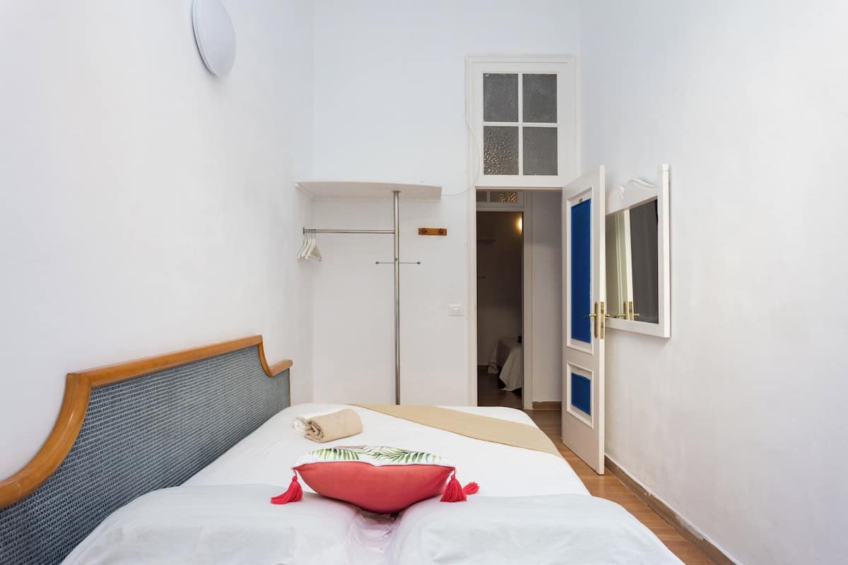 Un dormitorio con cama, ventana, puerta y un armario pequeño.