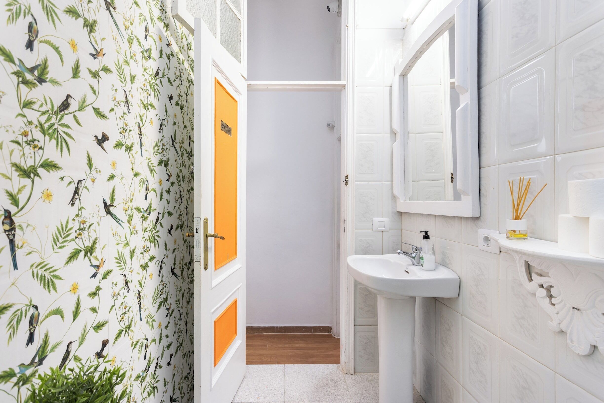 Een badkamer met een wit wastafel, een spiegel en een deur met een bloemen behangpatroon.