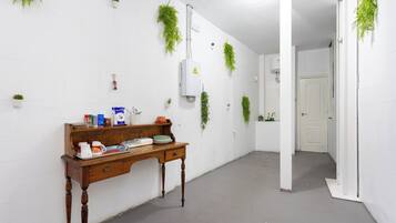 A hallway with a wooden desk, white walls, and hanging plants.