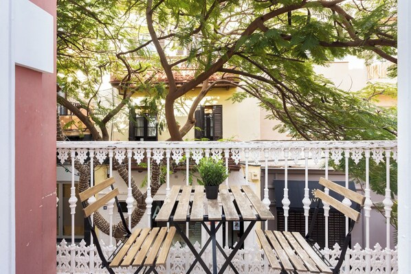 Un balcon avec une table et des chaises en bois, une plante en pot et une balustrade blanche décorative.
