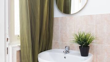 Un bagno con un lavandino bianco, uno specchio rotondo, una pianta in vaso e una tenda verde.