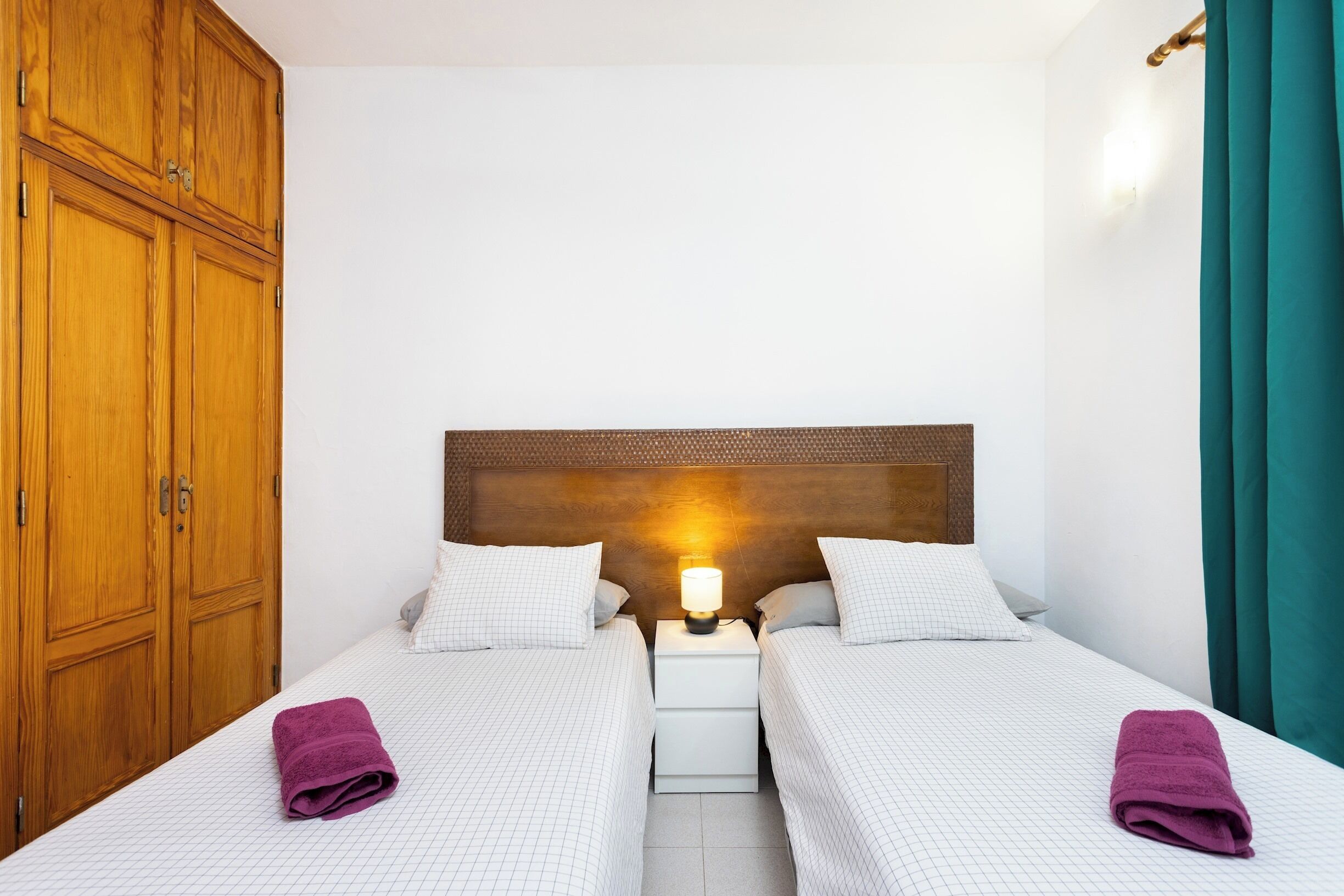 A double room with two beds, a nightstand, a wooden wardrobe, and a wall-mounted lamp.