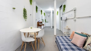 A narrow hallway with a white table and chairs, a bed with a checkered bedspread, and green plants on the walls. - Pensión Casablanca (Santa Cruz de Tenerife)
