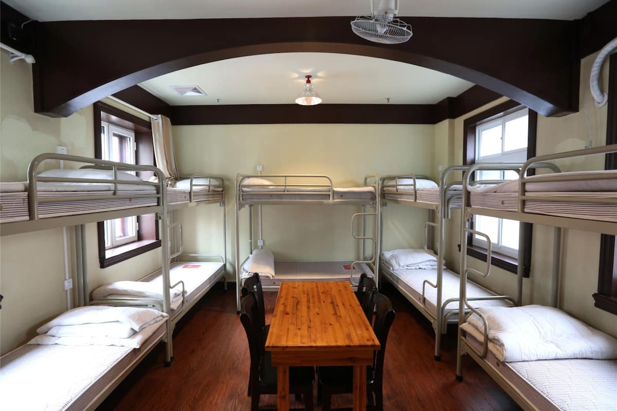 Une chambre avec des lits superposés, quatre lits en tout, une table en bois et un ventilateur de plafond.