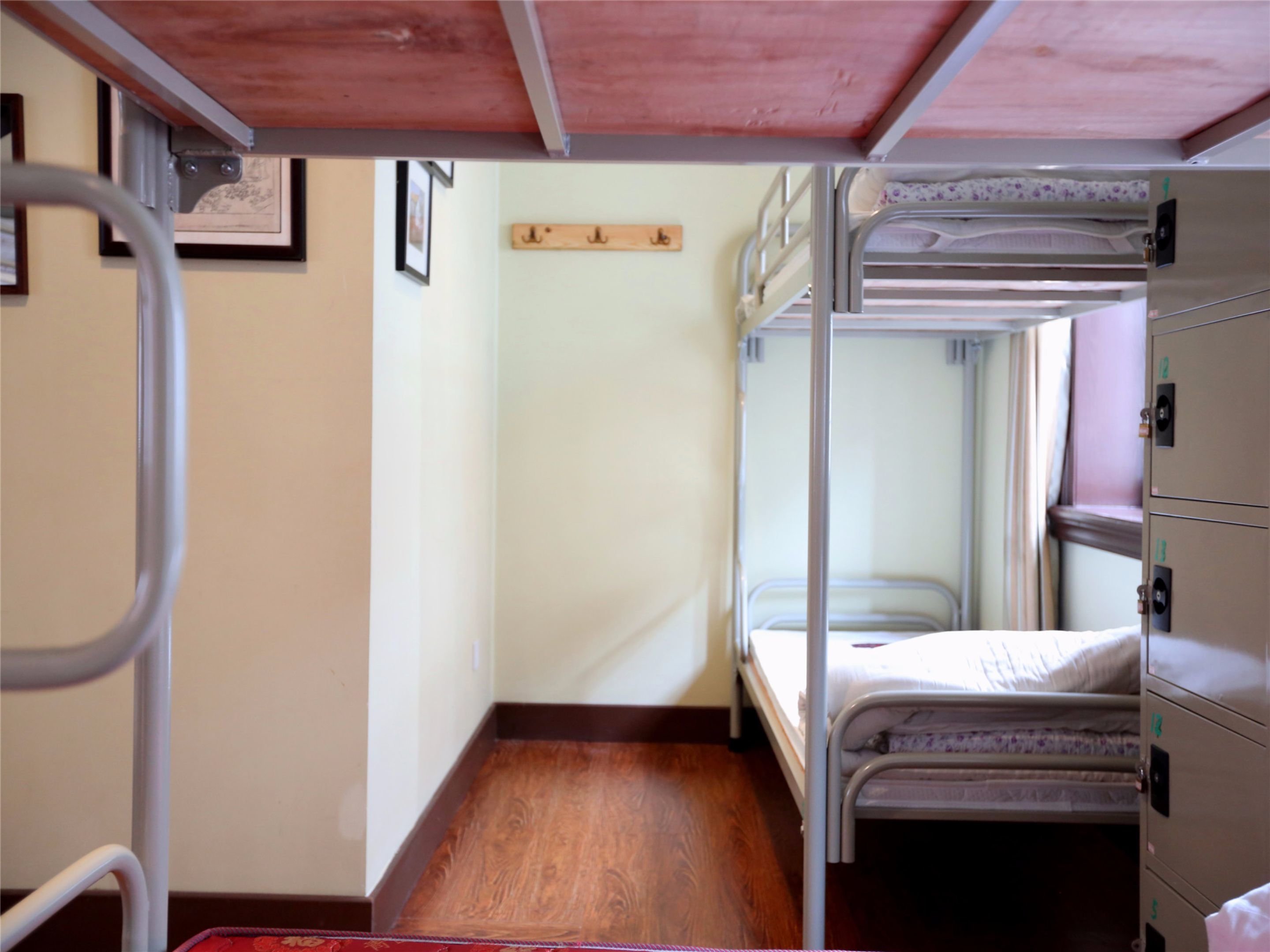 A narrow, single-bedded room with a wooden floor, metal bunk beds, and a metal wardrobe with numbered compartments.