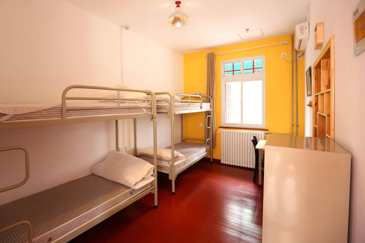 Une chambre de dortoir avec des lits superposés, un radiateur et une fenêtre avec des rideaux.