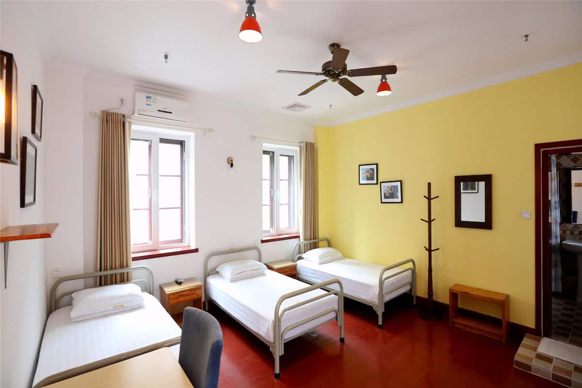 Une chambre d’hôpital avec deux lits, un bureau, une chaise, un porte-manteau et une fenêtre avec des rideaux.