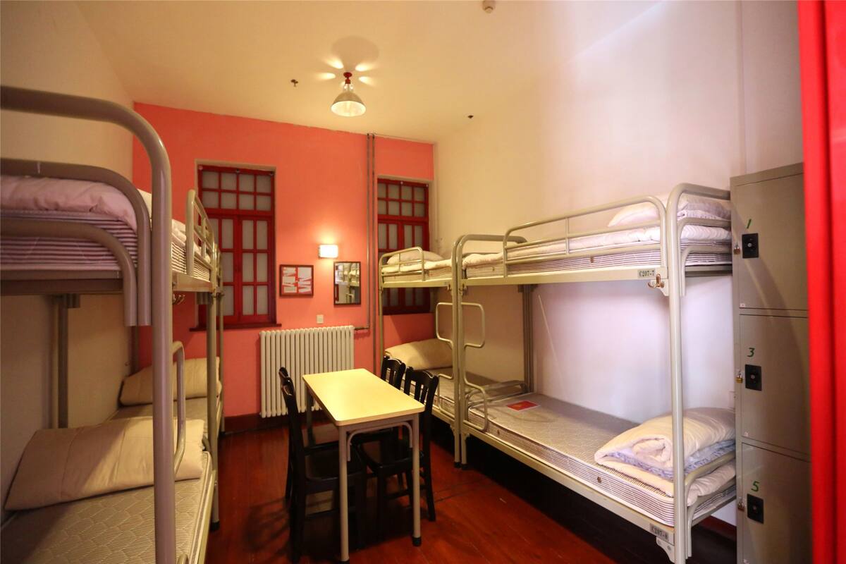 Une chambre de dortoir équipée de lits superposés, d’une table, de chaises, d’un radiateur et d’un ventilateur de plafond.
