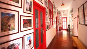A hallway with framed pictures on the walls, a red door, and a wooden bench. - Qingdao Wheat Youth Hostel (Qingdao)