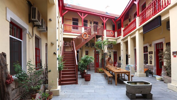 A courtyard with a wooden staircase, potted plants, a stone bench, and a dining table. - Qingdao Wheat Youth Hostel (Qingdao)