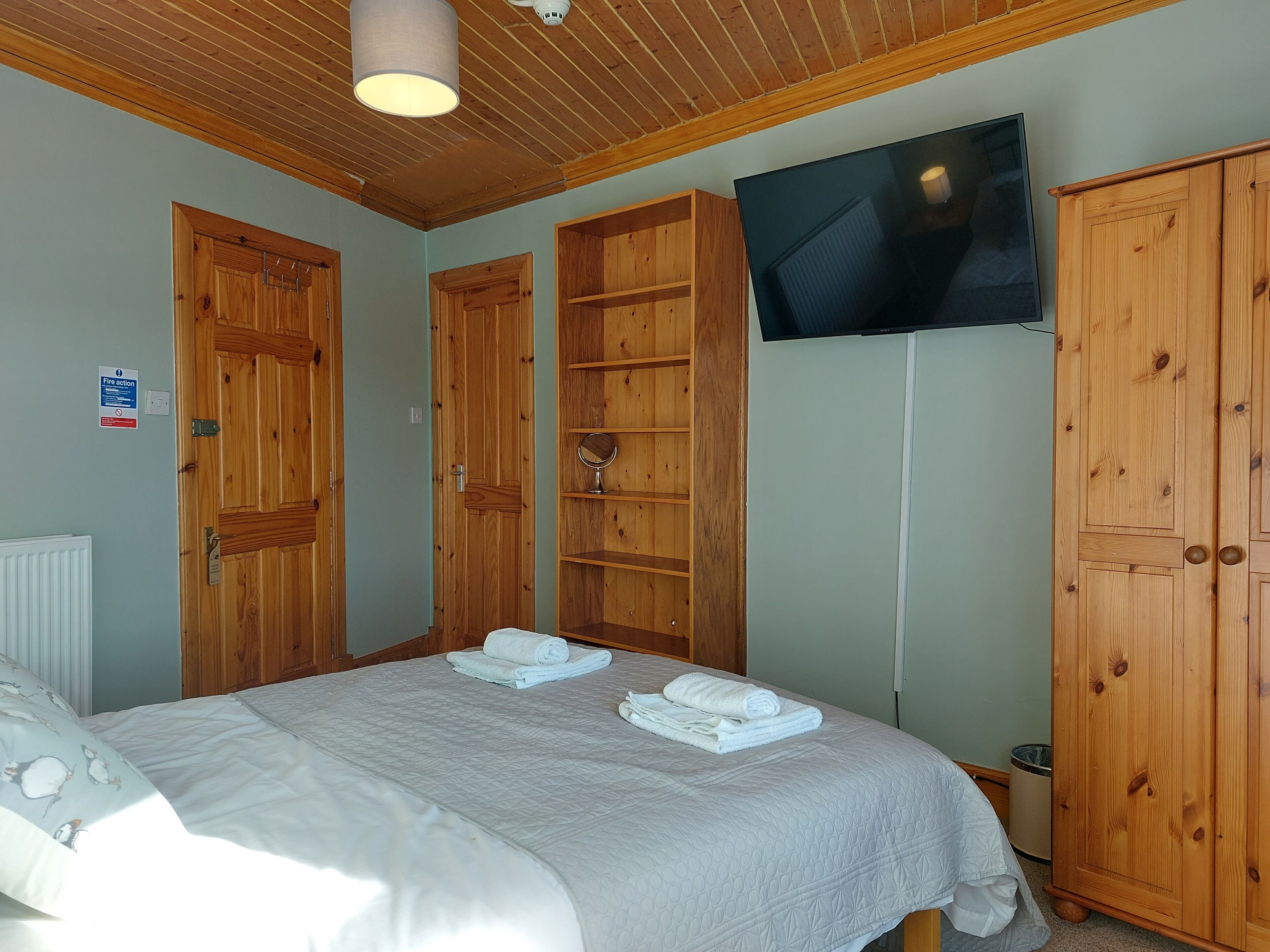 A bedroom with a bed, wooden wardrobe, and a television on the wall.