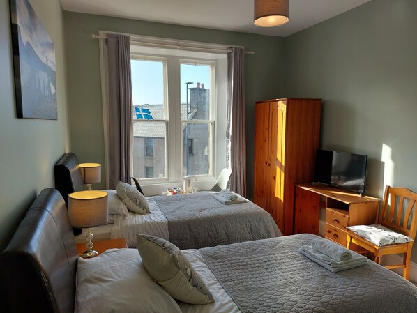 A bedroom with two beds, a desk, a TV, and a wardrobe.