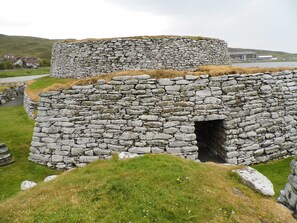 A stone structure with a circular entrance, surrounded by grass and a few scattered rocks. - Eddlewood Guest House (Lerwick)