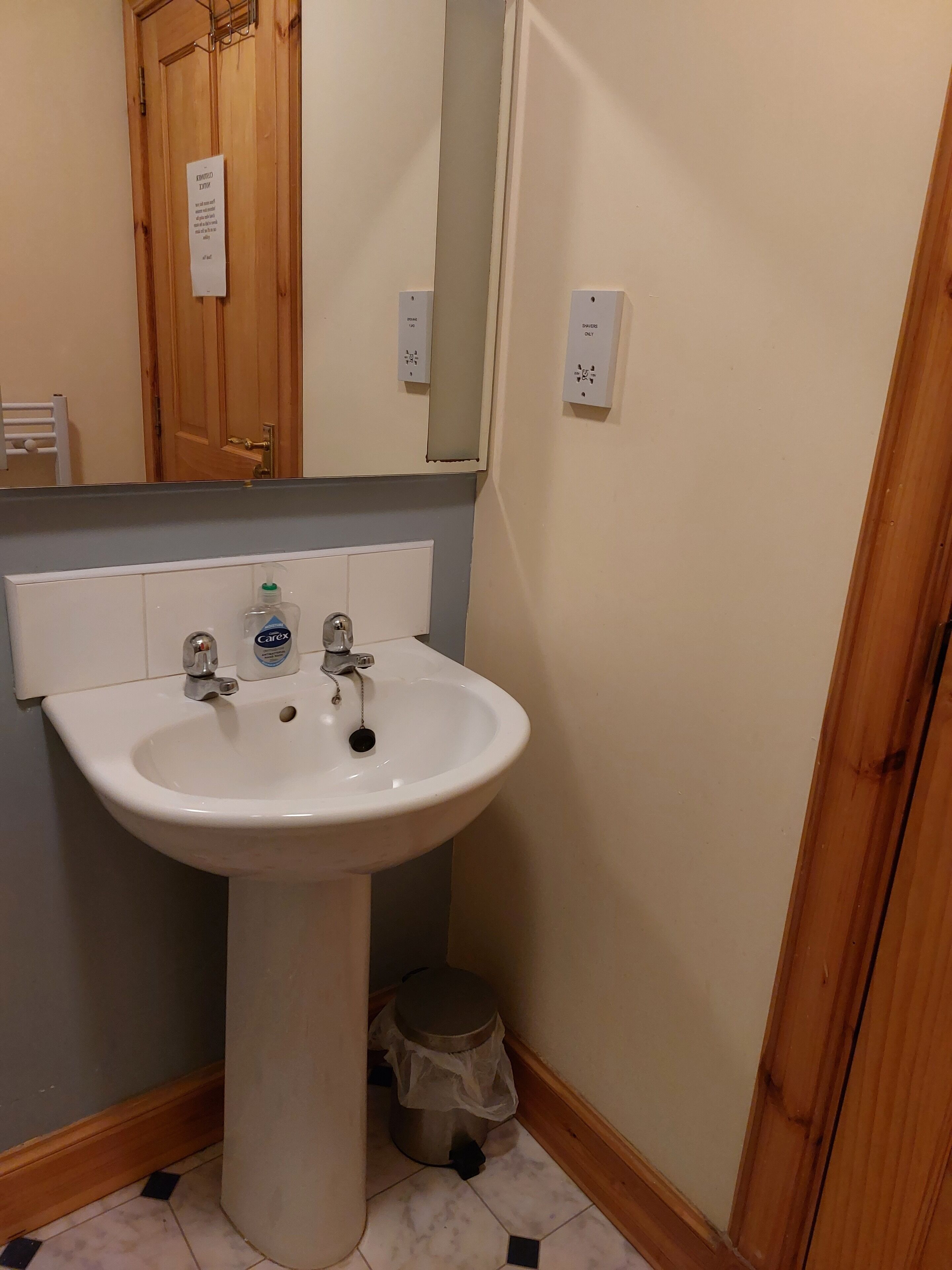 Een badkamer met een witte wastafel, een spiegel en een houten deur.