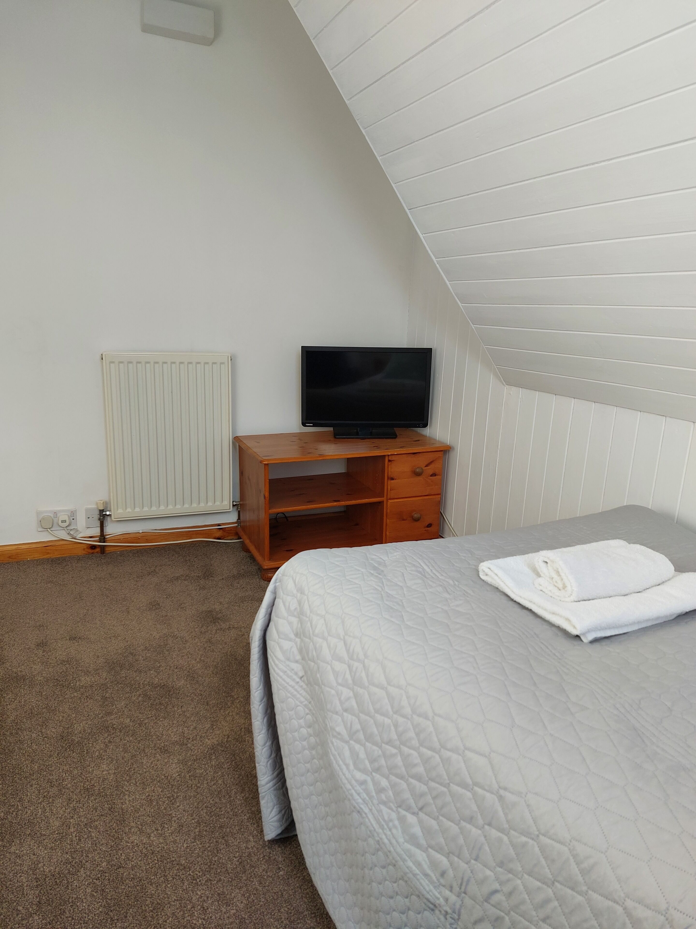 A bedroom with a bed, a wooden nightstand, a television, and a radiator.