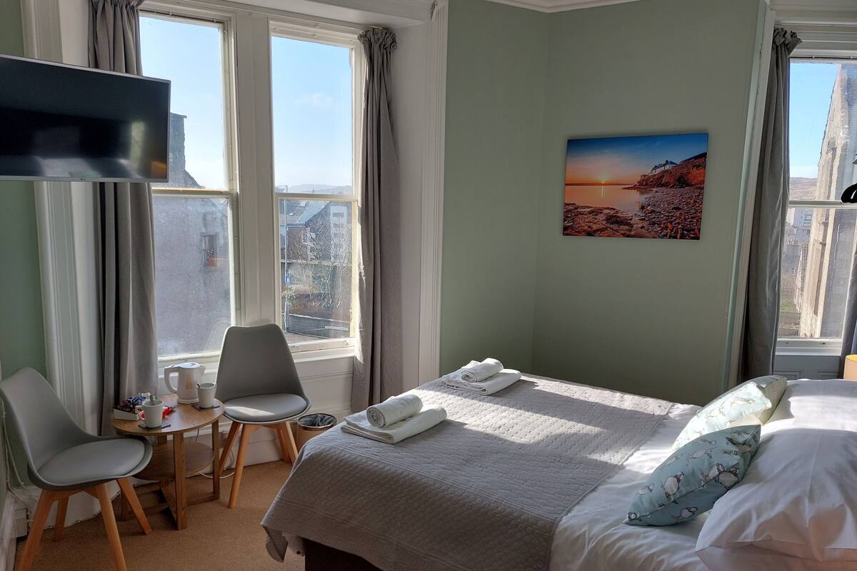 Ein Hotelzimmer mit einem Bett, einem Sessel, einem kleinen Tisch mit Wasserkocher und einem Bild an der Wand.