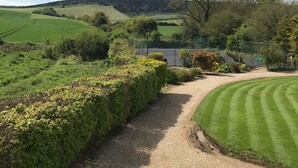 A gravel path leading to a green lawn area with a tennis court in the background. - Shepherds Barn (Chichester)