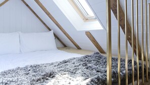 A bedroom with a sloped ceiling, a skylight, a bed with white bedding, and a fluffy gray rug. - Shepherds Barn (Chichester)