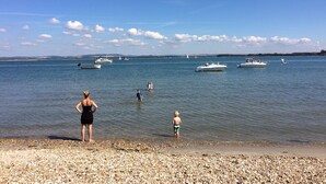 A pebbled beach with boats on the water and a clear sky. - Shepherds Barn (Chichester)