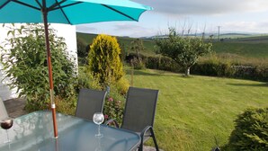 An outdoor patio with a glass table, two chairs, a blue umbrella, and a wine glass. - Bluebell Bank (Dumfries)