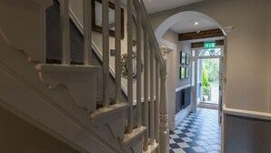 Una escalera con balaustres blancos y piso a cuadros que lleva a un vano con una señal de salida verde.