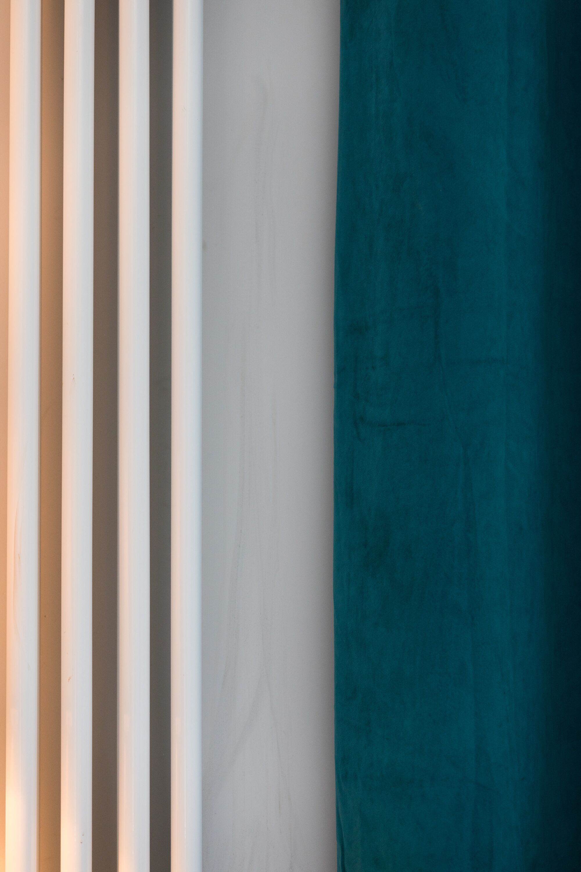 A room with a teal curtain, a white wall, and a window with vertical blinds.