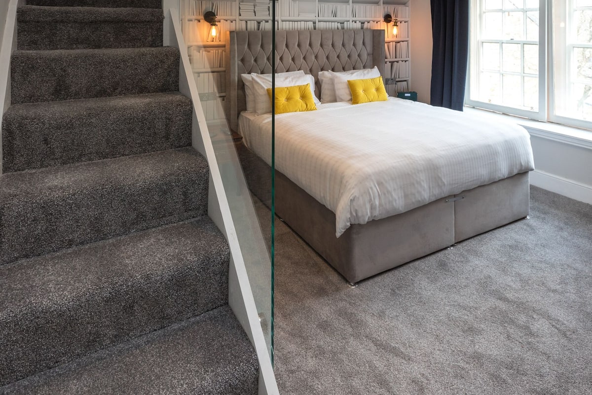 A bedroom with a large bed, a glass-enclosed staircase, and a view of a balcony.