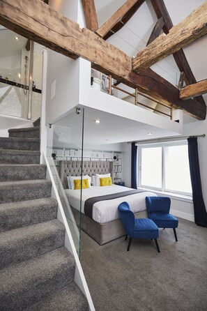 Een moderne slaapkamer met een bed, twee blauwe stoelen, een trap en een groot raam.