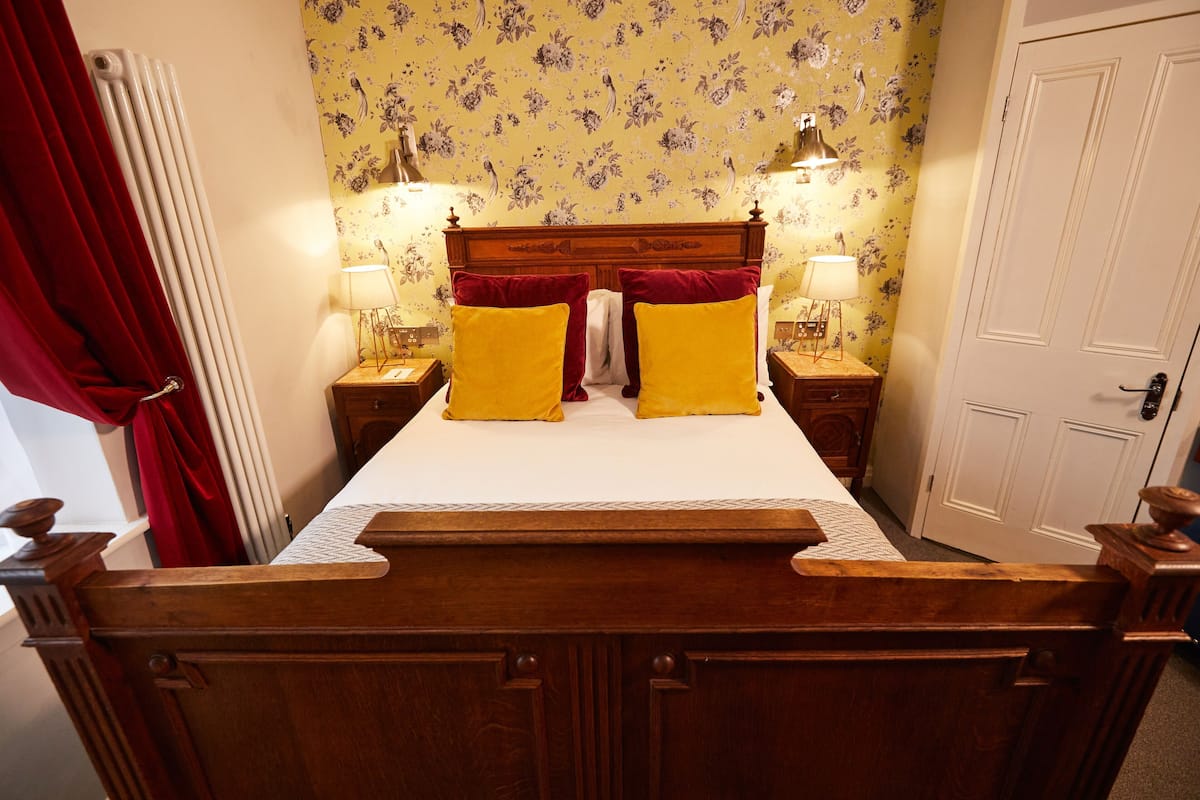 A bed with a wooden headboard, two bedside lamps, and a floral wallpaper pattern.