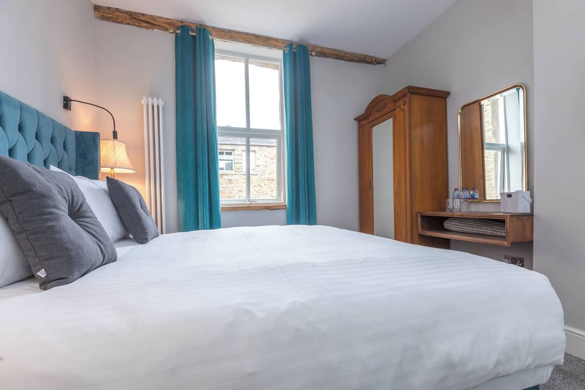 A neatly made bed with a headboard, a bedside lamp, a wooden wardrobe, and a window with curtains.