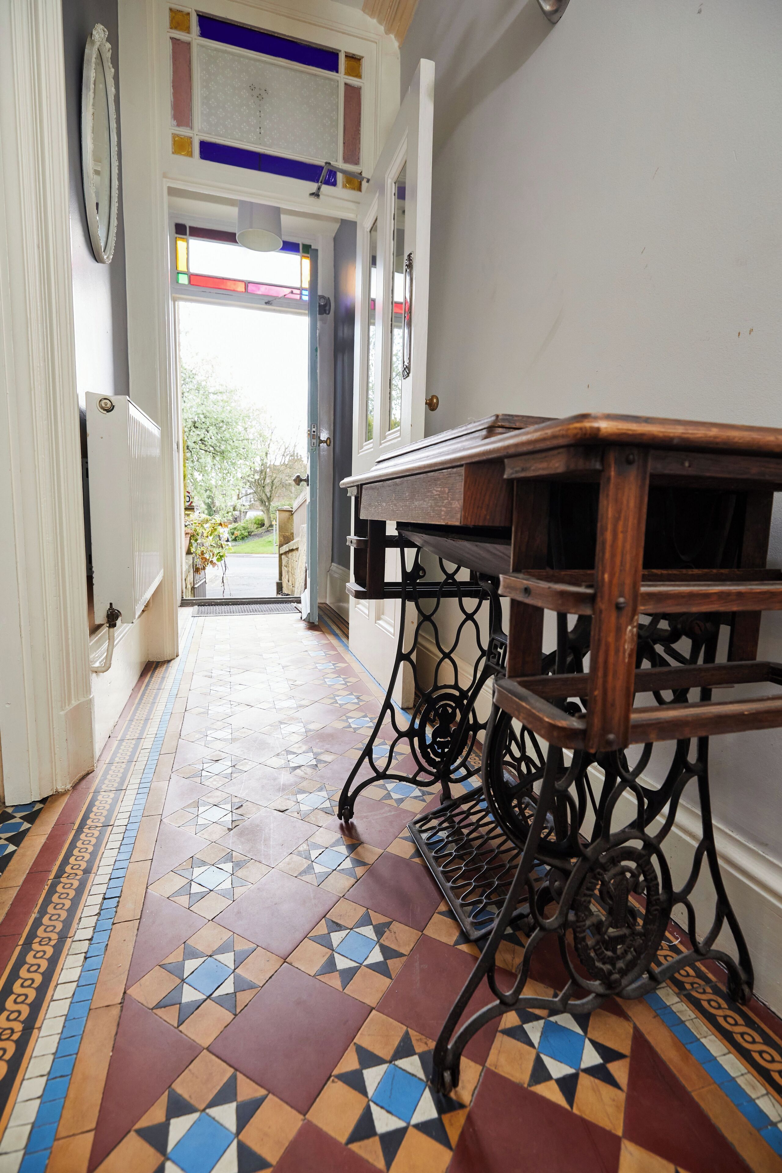Un pasillo con suelo de baldosas, una mesa de madera y una puerta que da al exterior.