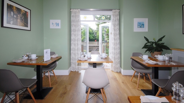 A dining area with two tables, chairs, and a view through a glass door. - Abbey Guest House (York)