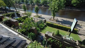 A riverside garden with a paved walkway, benches, and a signboard. - Abbey Guest House (York)