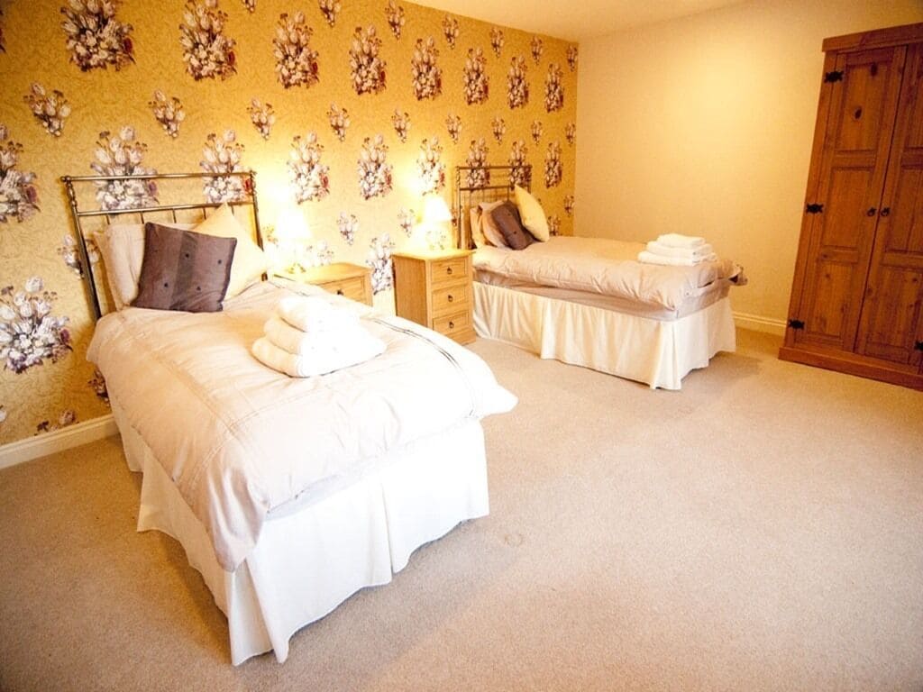 A bedroom with two beds, a wooden wardrobe, and a floral wallpaper.