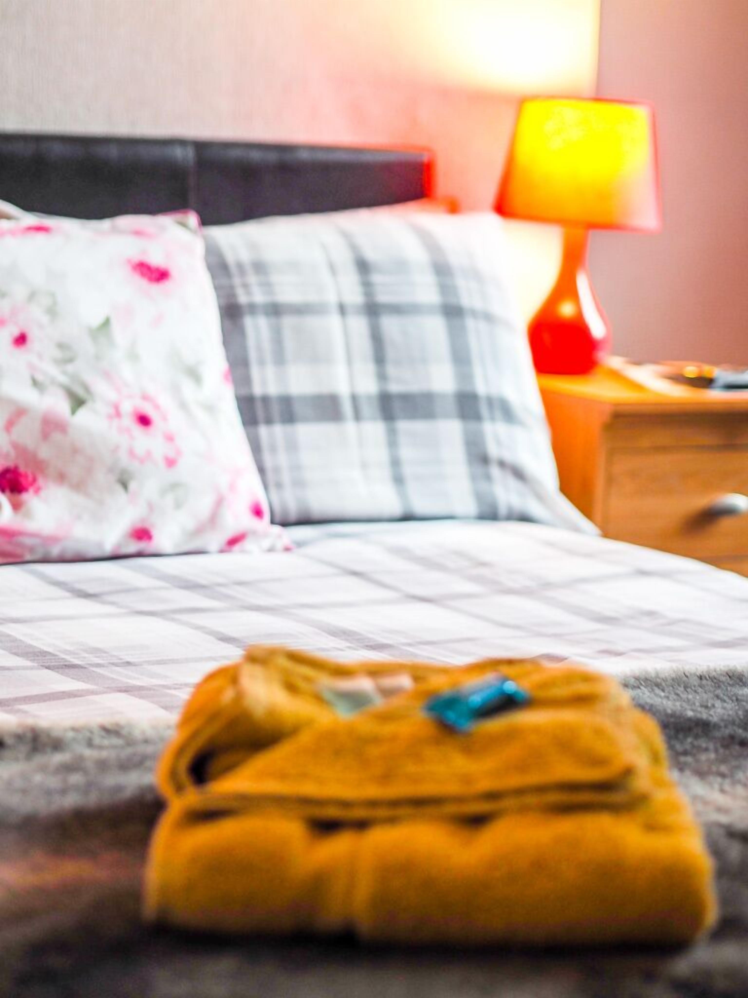 Un lit avec une couvre-lit à carreaux, un coussin à motifs floraux et une lampe sur une table de chevet.