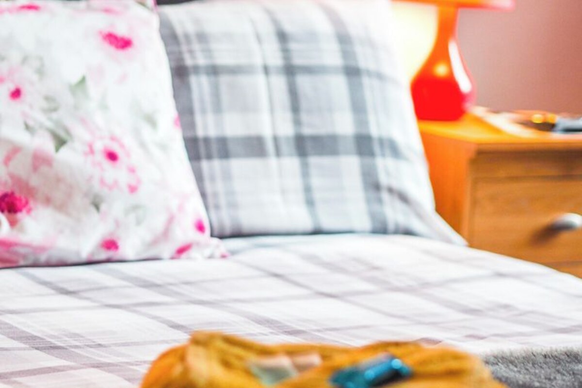 A bed with a floral pillow, a plaid pillow, and a yellow bag on the bed.