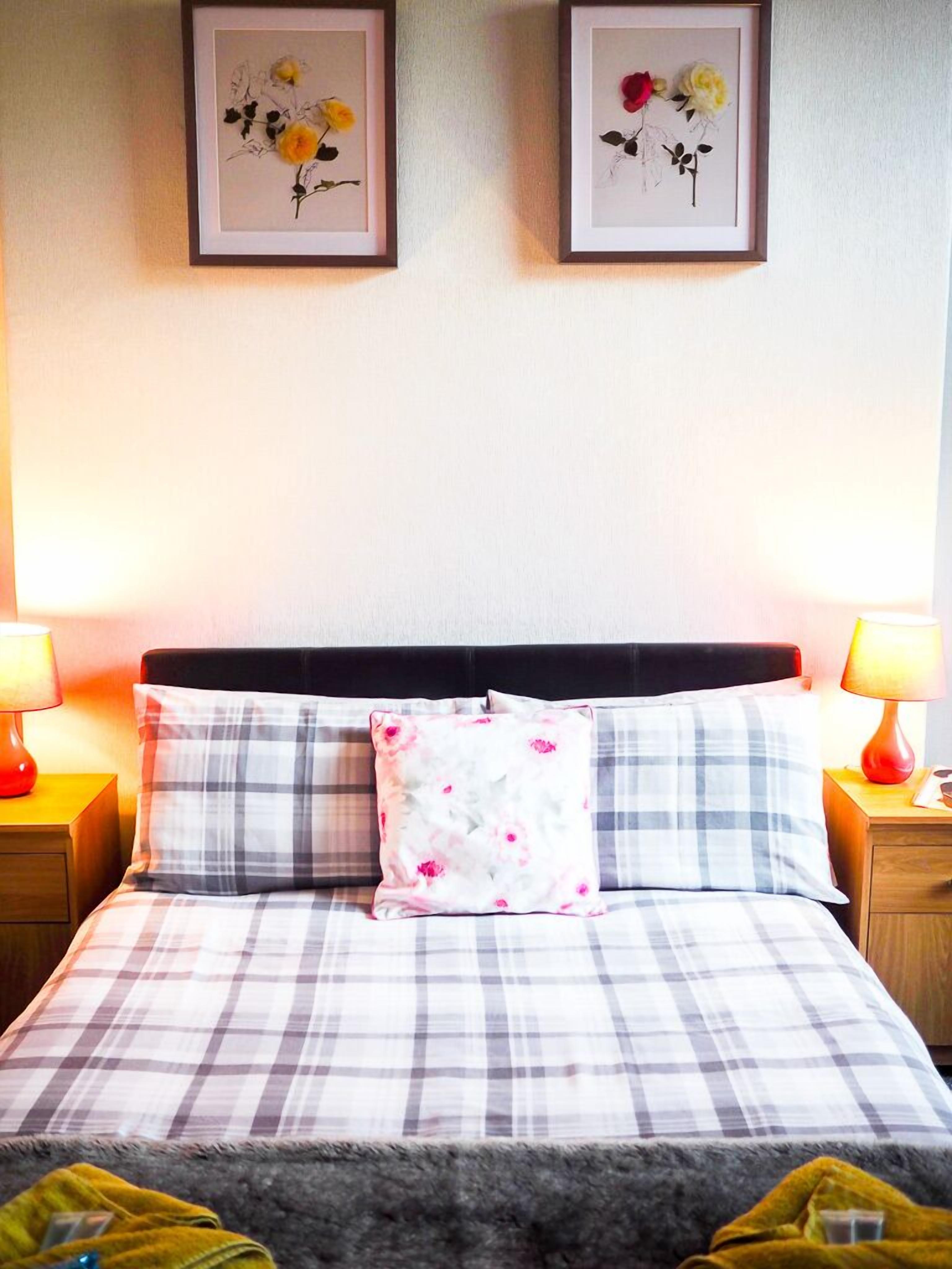 A neatly made bed with a plaid bedspread and two pillows, flanked by nightstands with lamps.