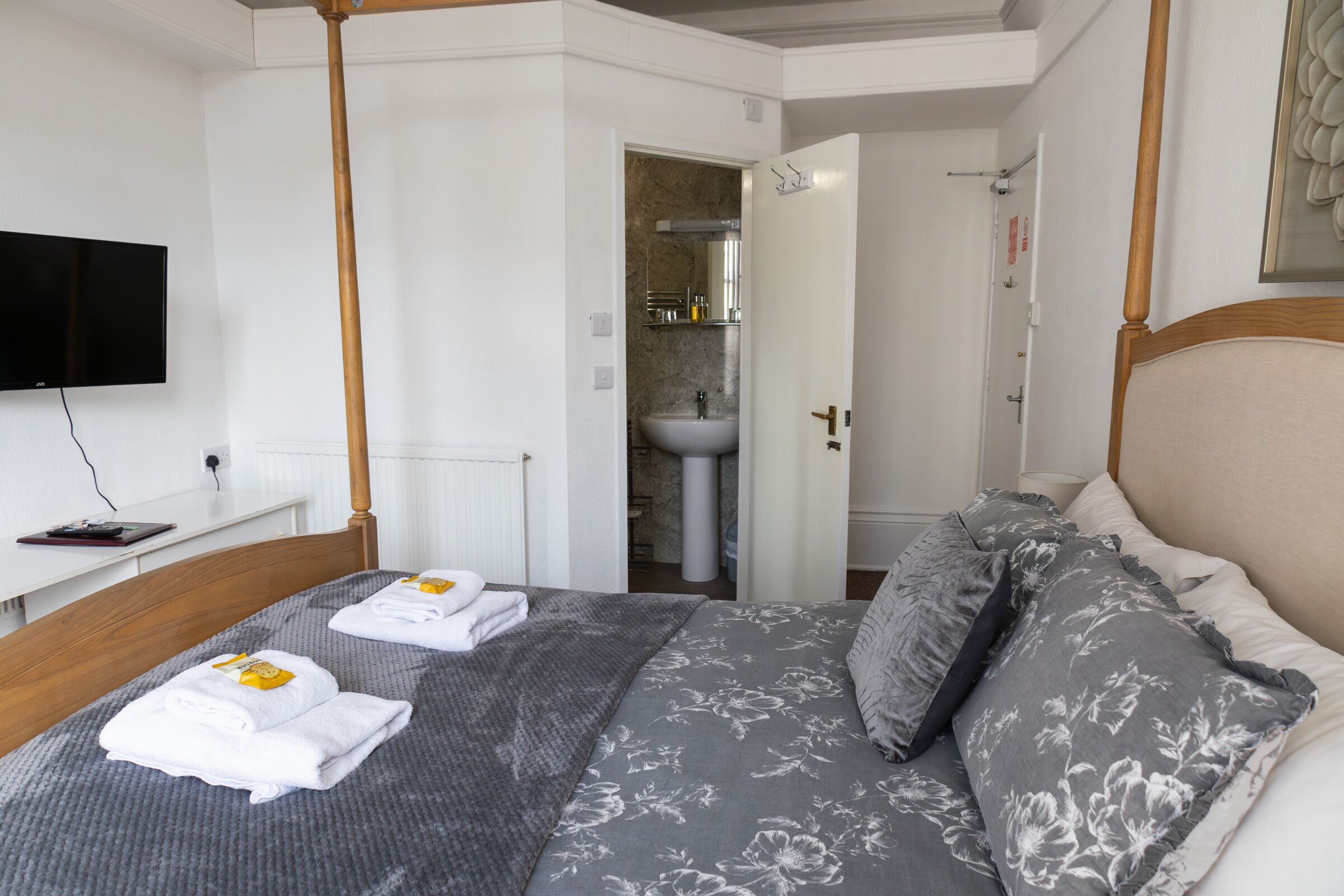 A bedroom with a bed, a television, a bathroom visible through an open door, and a bedside table with a book.