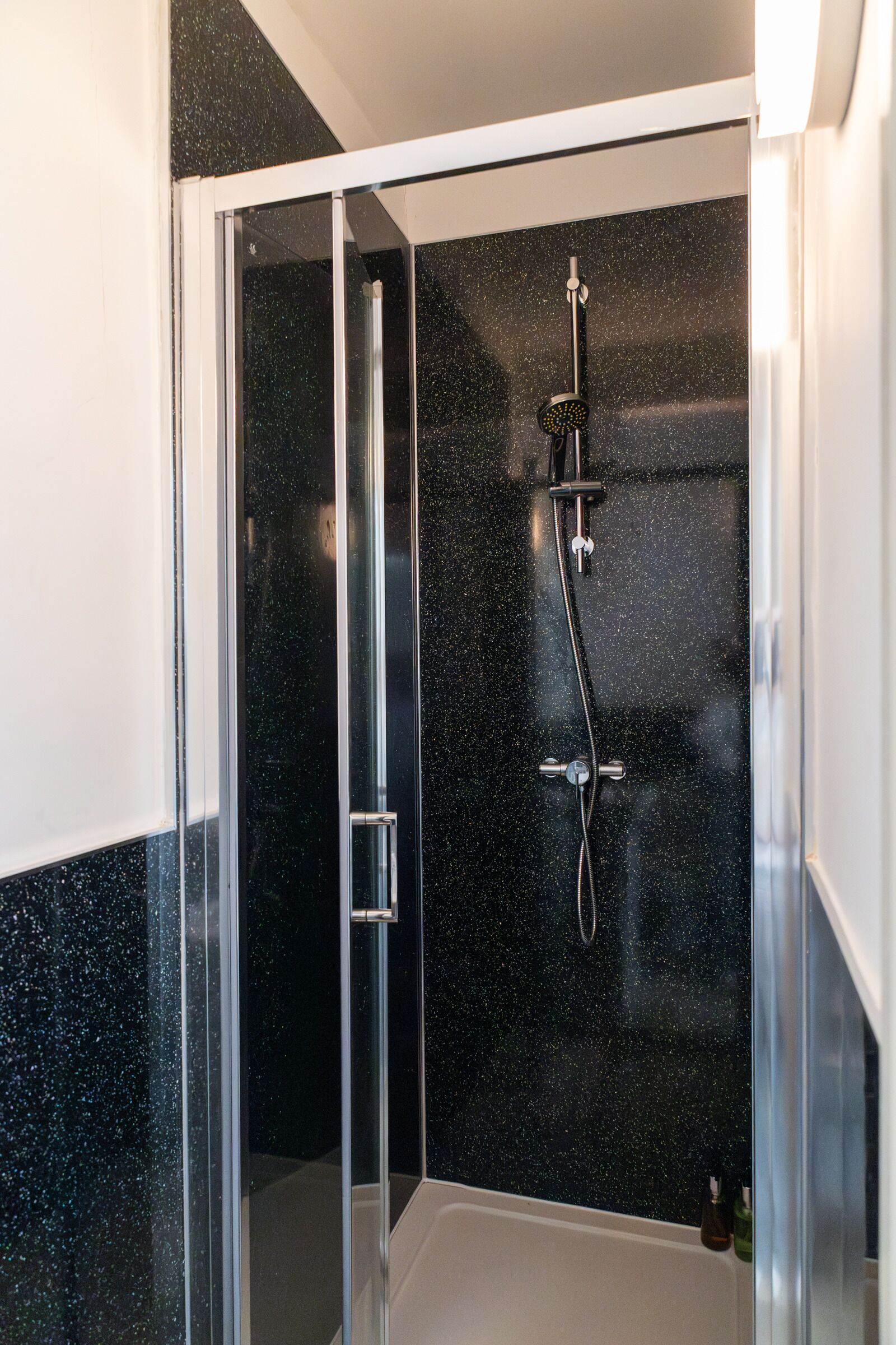 A glass-enclosed shower with a black speckled wall, a chrome showerhead, and a handheld showerhead.
