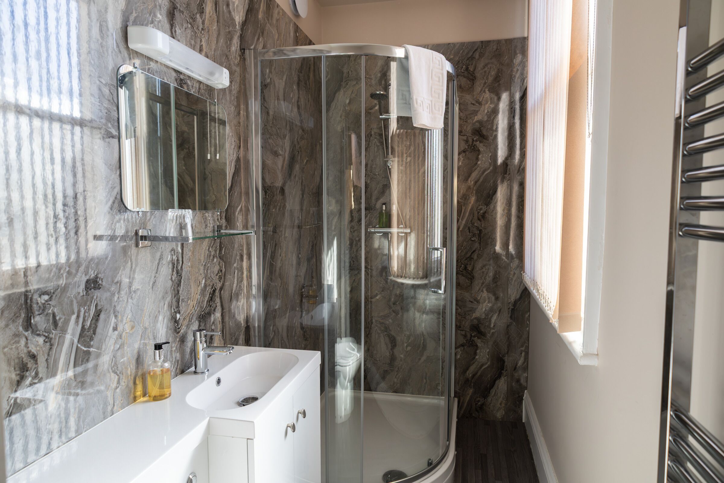 A modern bathroom with a glass-enclosed shower, a white sink, and a marble wall.