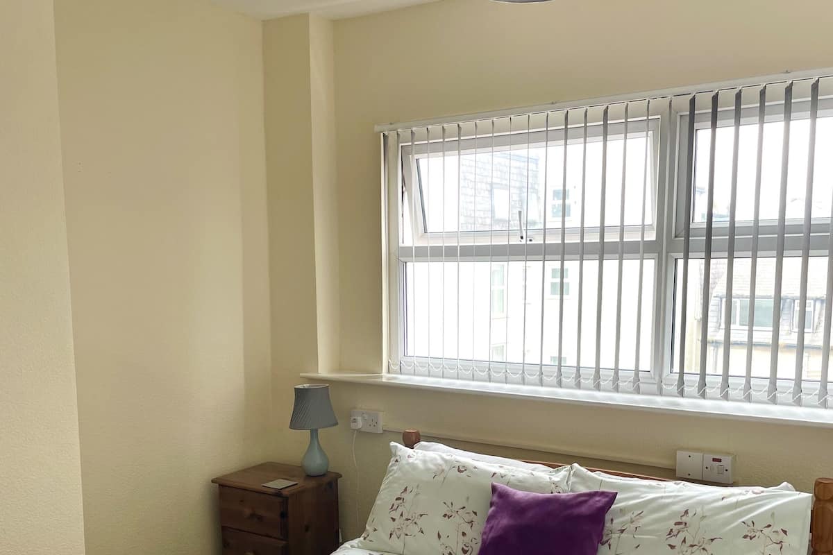 A bedroom with a bed, a nightstand, a lamp, and a window with blinds.