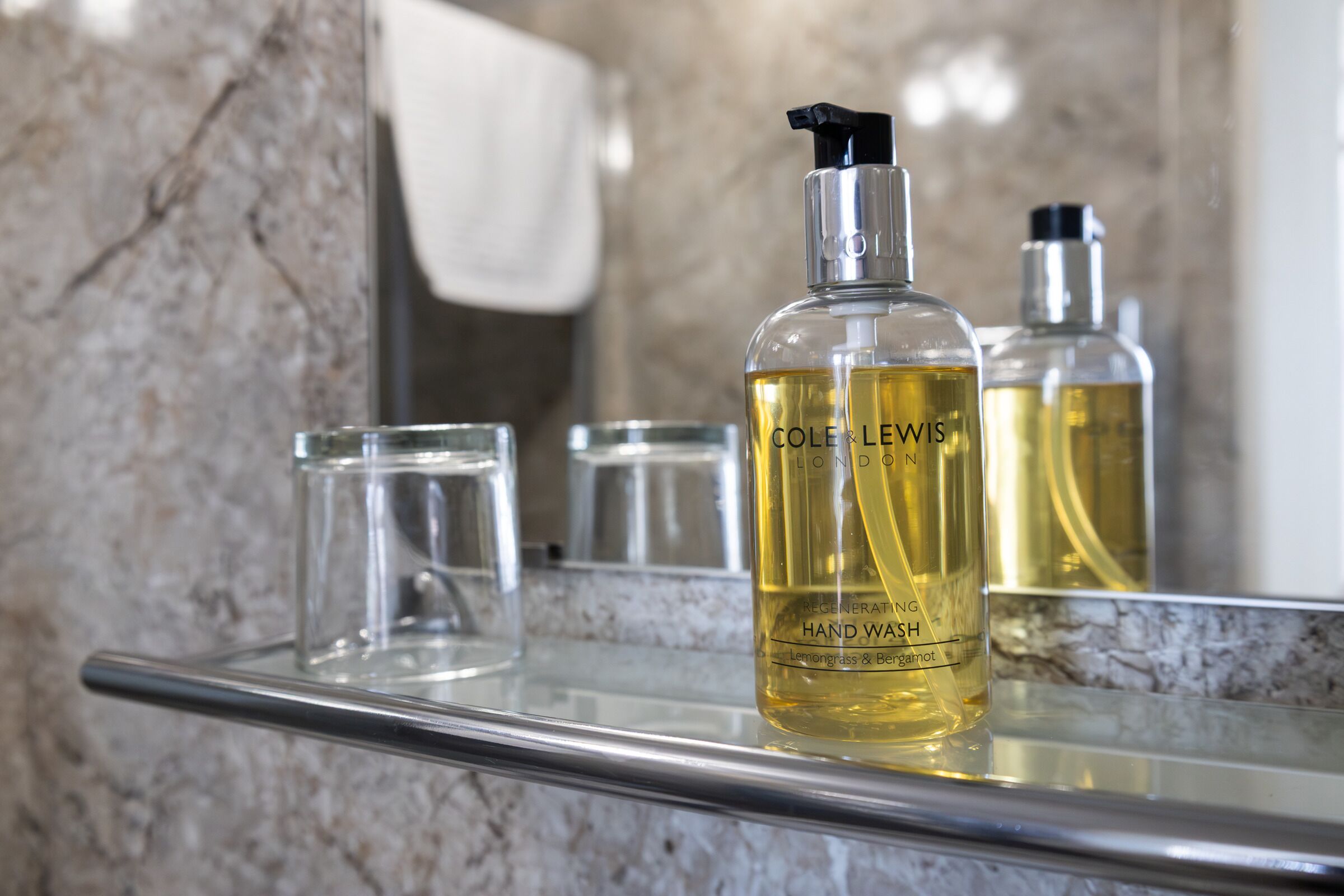 A bathroom with a marble countertop, a bottle of Cole Lewis hand wash, and a glass.