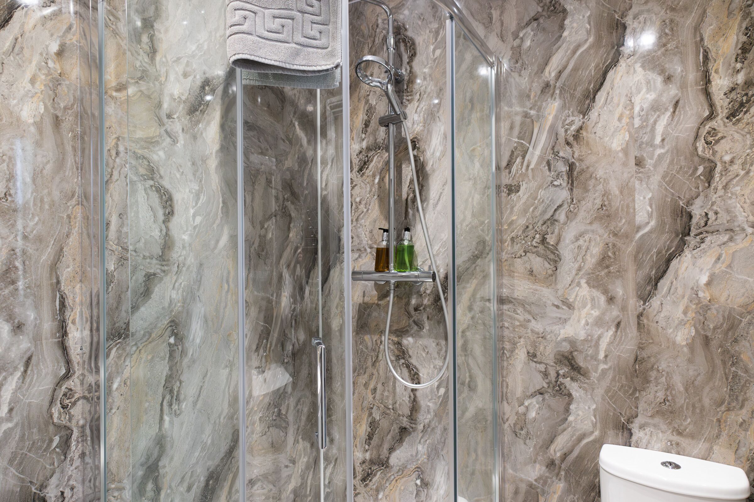 A bathroom with a glass-enclosed shower, marble walls, and a toilet.