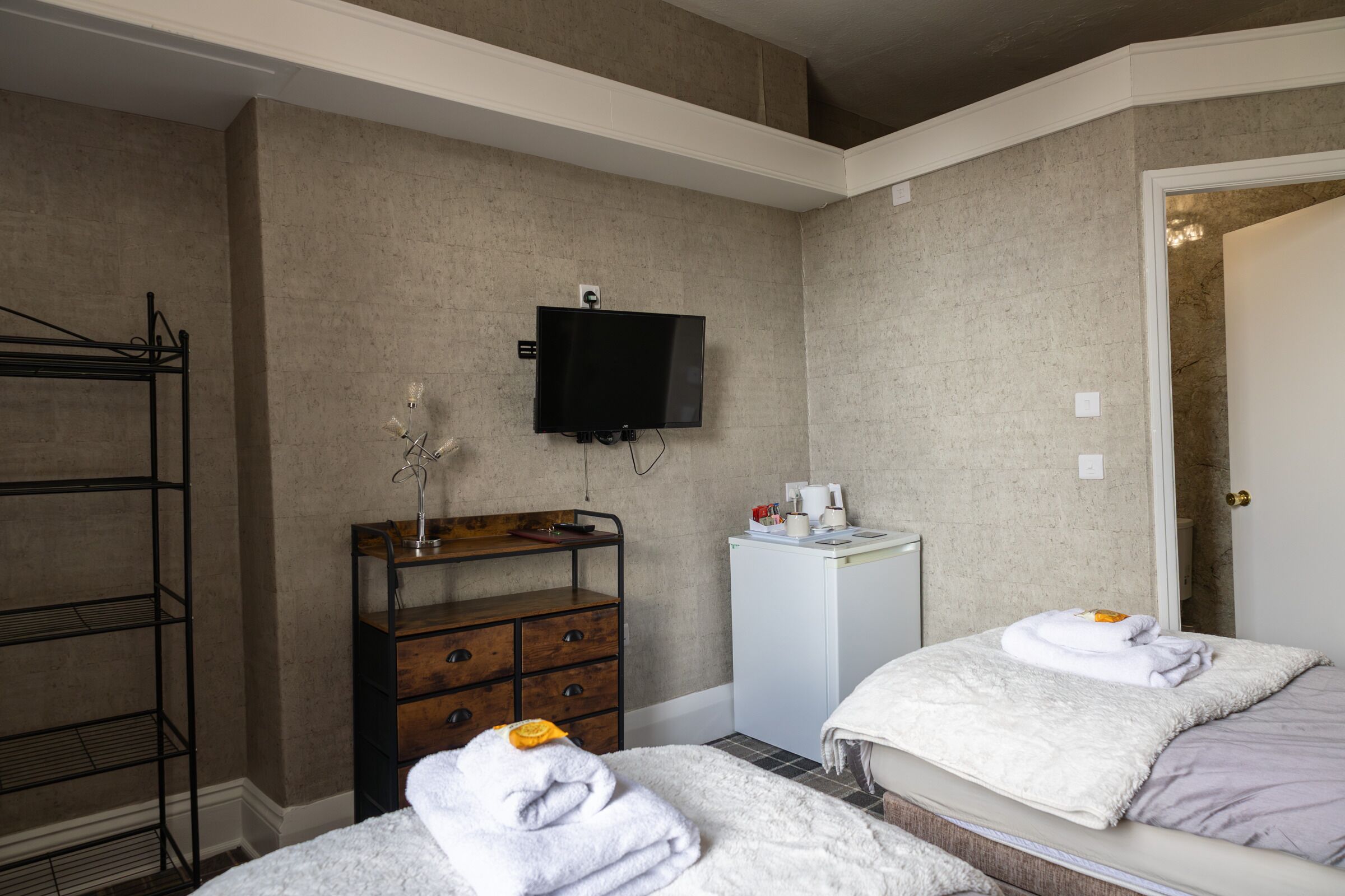 A hotel room with a bed, a TV mounted on the wall, a small desk with a mirror, and a wardrobe.