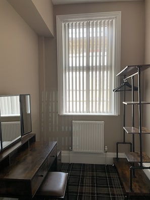 A room with a large window, a radiator, a wooden bench, a mirror, and a metal shelf. - Carlton House Guesthouse (Scarborough)