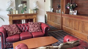 A spacious lobby with a red leather sofa, a wooden reception desk, and a mirror reflecting the room. - Carlton House Guesthouse (Scarborough)