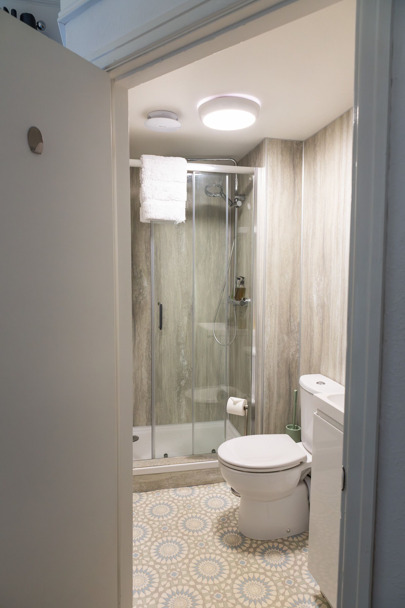 A bathroom with a glass-enclosed shower, a toilet, and patterned floor tiles.