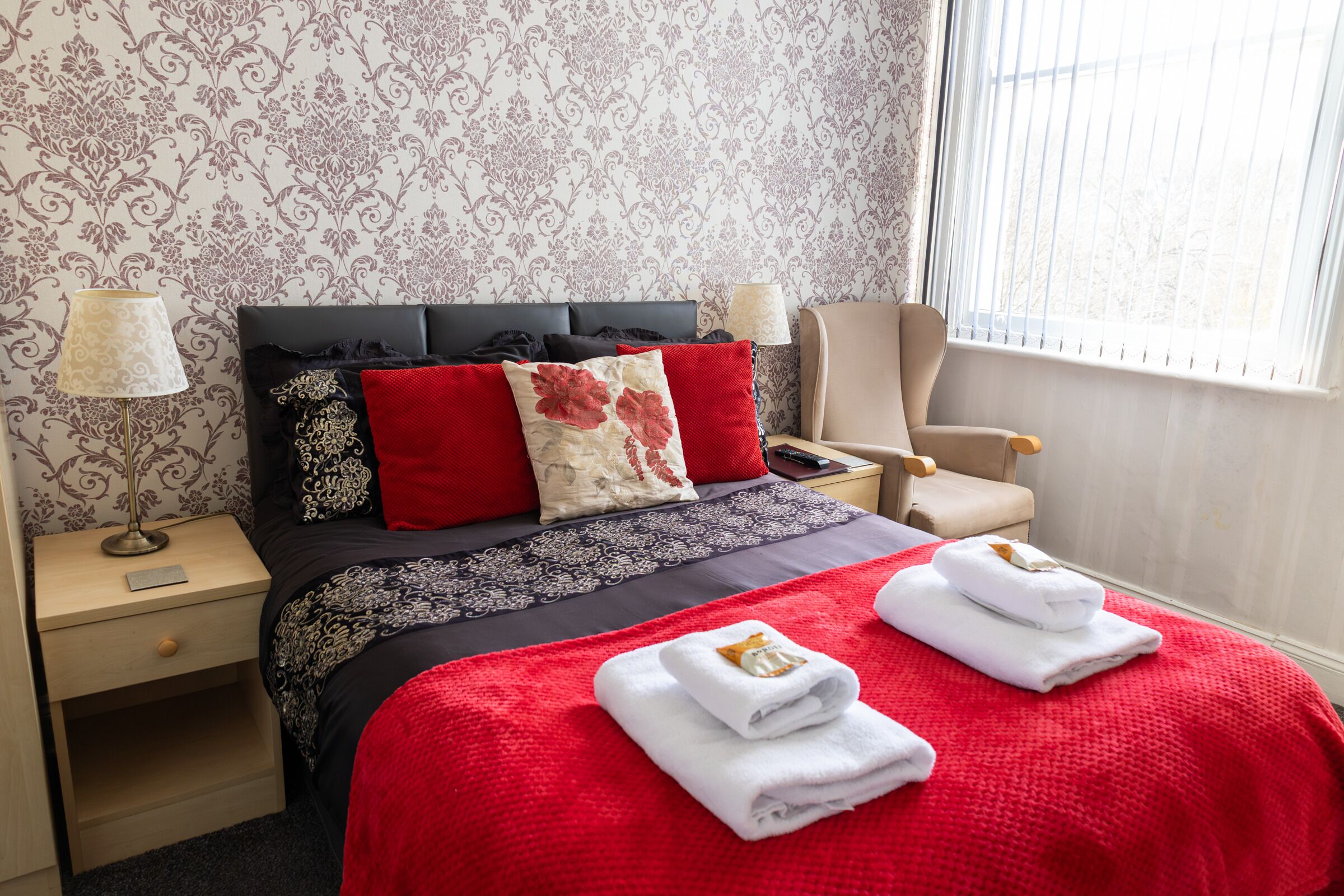 Une chambre d’hôtel avec un lit, une chaise, une table de chevet et une fenêtre.