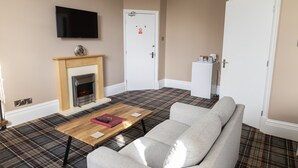 A living room with a sofa, a fireplace, a television, and a door with a sign. - Carlton House Guesthouse (Scarborough)
